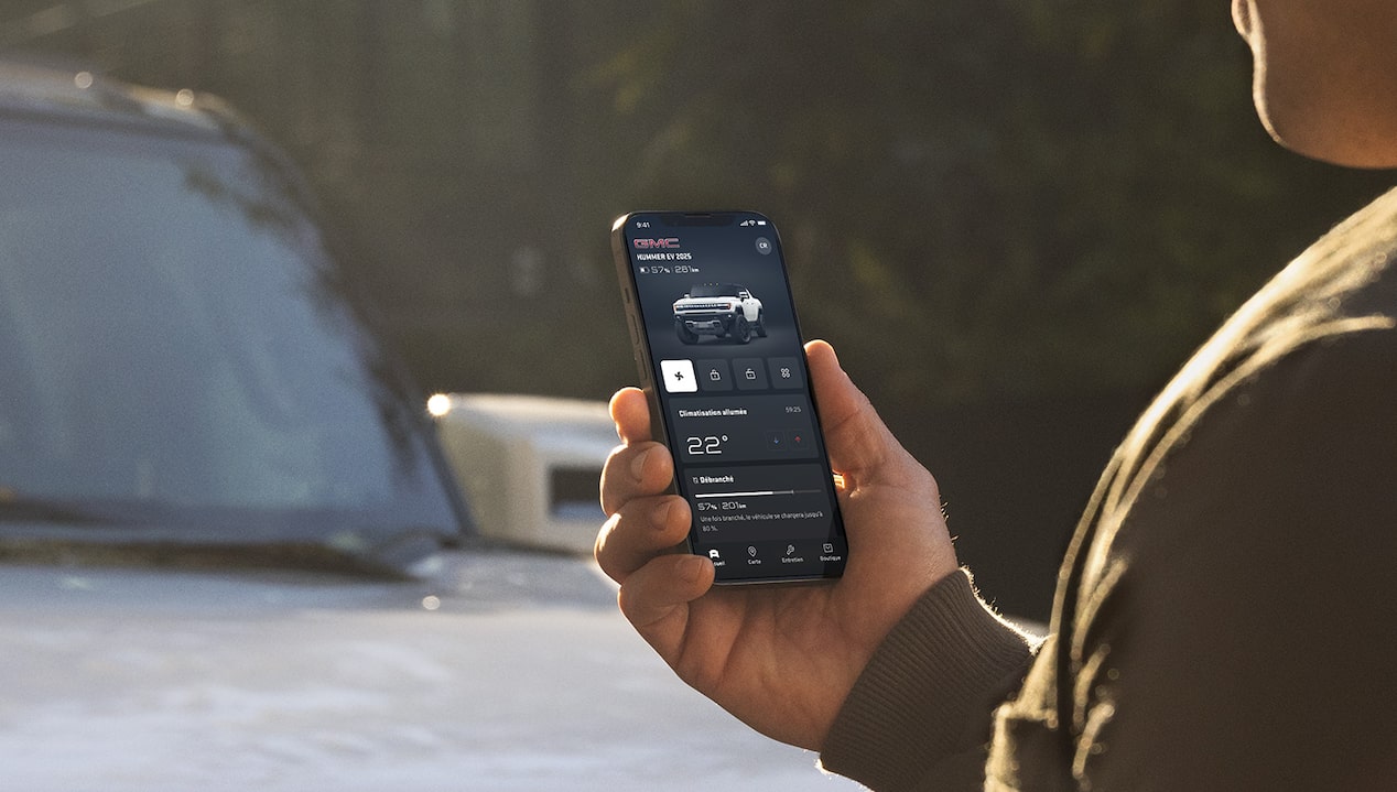 Une personne utilise l’appli mobile du VUS GMC Hummer EV 2025 sur son téléphone devant un véhicule stationné.