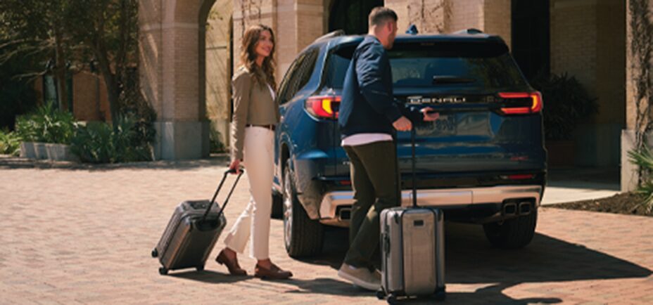 A Woman and a Man Approach a Parked GMC Denali with Rolling Suitcases