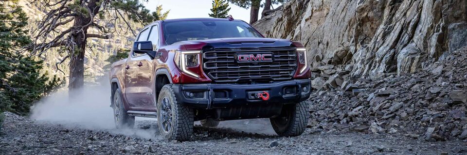 A GMC Sierra 1500 AT4 Truck Kicking Up Dust While Driving on a Gravel Path Next to Mountains