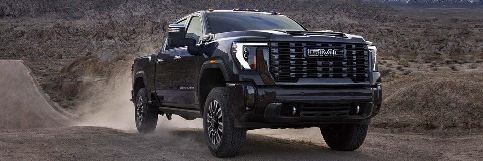 Front Three-Quarters View of a GMC Sierra HD Denali Truck Kicking Up Dust Driving on a Dirt Path Through the Mountains