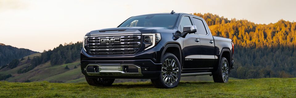 Wide Front Three-Quarters View of a GMC Sierra 1500 Denali Truck Parked in Front of Mountains at Sunset