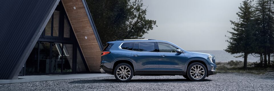 Profile View of a Blue GMC Acadia Parked Next to a Beautiful Cabin in the Woods