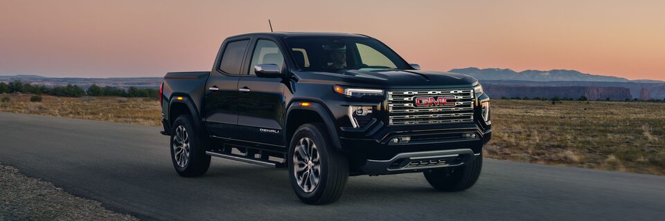 A Black 2025 GMC Canyon Denali Driving Down a Road During a Sunset