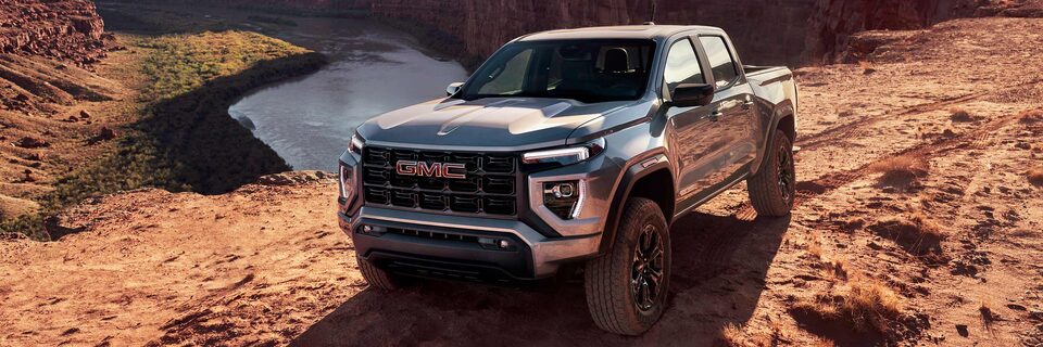 Two 2025 GMC Canyon Trucks Parked in the Desert with Snow Melting in the Background