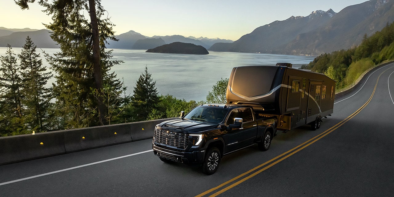 Wide View of a 2026 GMC Sierra HD Denali Hauling a Trailer near the Lake During a Sunset